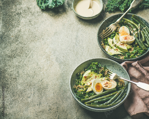 Healthy vegetarian breakfast bowls. Quinoa, kale, green beans, avocado, egg and tahini dressing bowls over concrete background, selective focus, copy space. Energy boosting, diet food concept