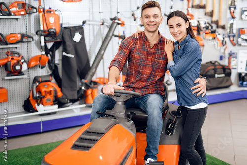 A young couple is sitting on a lawn mower.