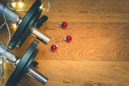 Obraz na płótnie Top view of black metal fitness weights on wooden background with shining Christmas lights and red decorations, holidays and fitness concept w salonie