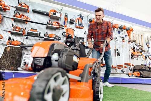 A guy is posing with a lawn mower in a tool store. © VadimGuzhva
