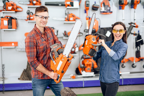 A guy and a girl are posing on the camera with chainsaws in their hands. photo