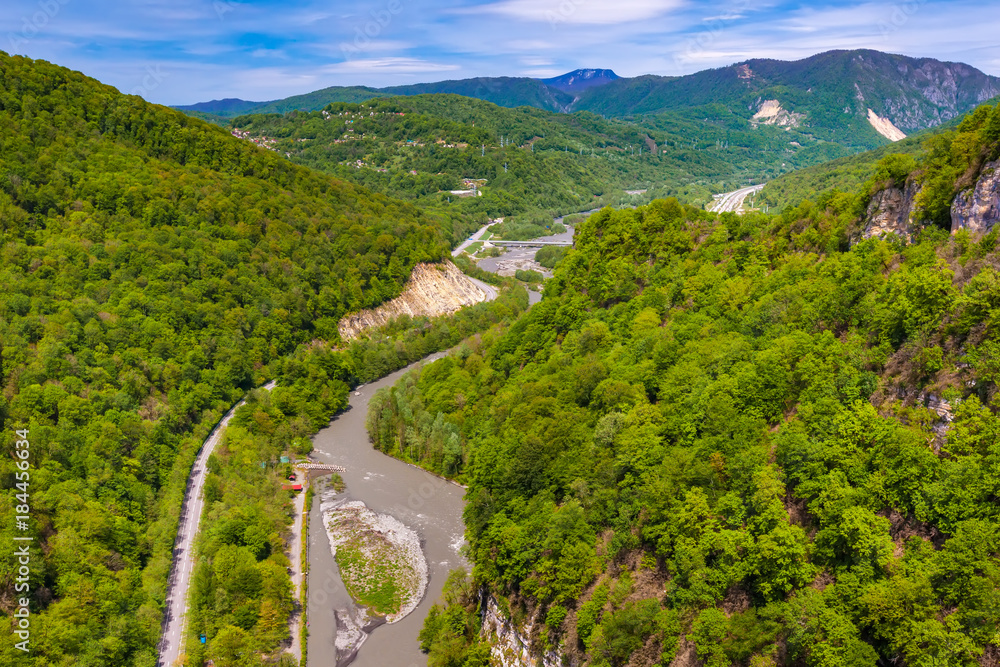 Fototapeta premium A colorful spring green forest on the slopes along the banks of the Mzymta River flowing near the road. Mountain valley on the way to Krasnaya Polyana from Adler, Sochi, Russia.