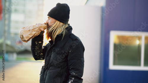 Fotografie Drunk homeless man with drink alcohol from paper bag while standing at the city