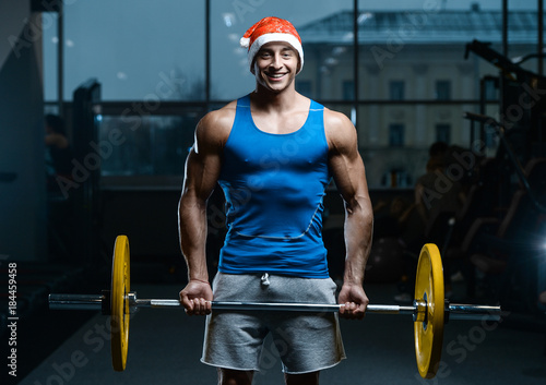 Bodybuilder young handsome santa clause smile in red santa hat train muscles