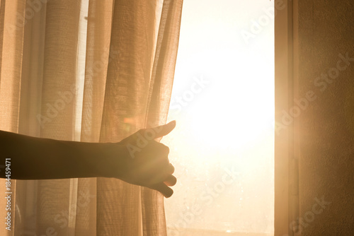 Female arm reaching out to open a curtain - warm sun light shining through