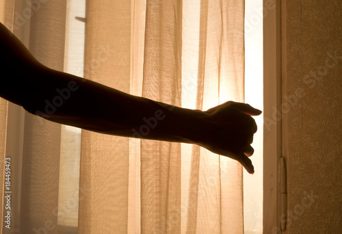 Female arm reaching out to open a curtain - warm sun light shining through. New beginning, possibilities, mystery, looking into the light, morning