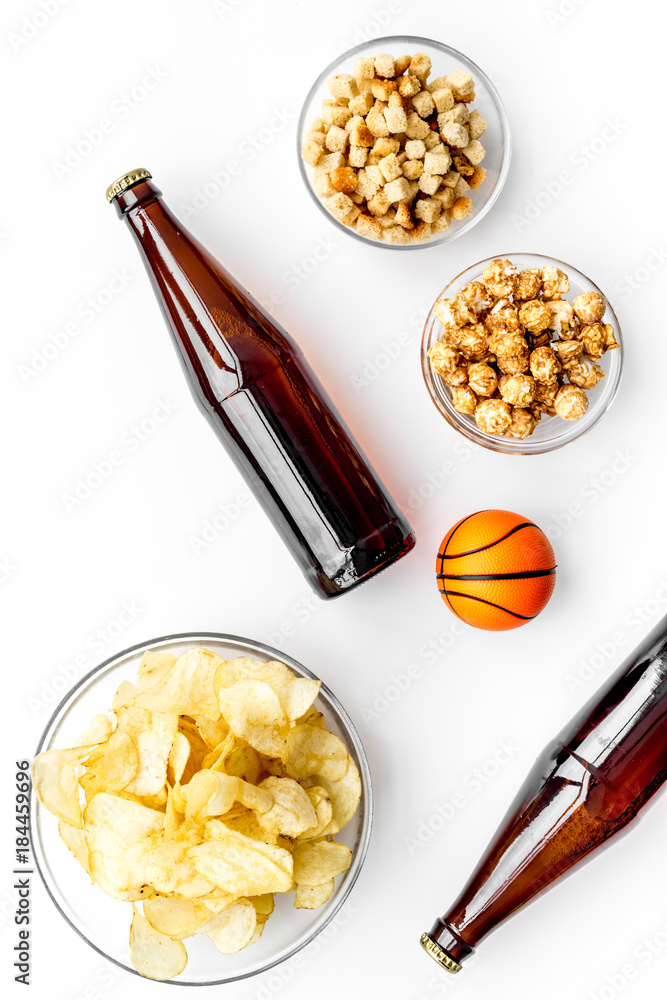 Snacks for watching sport matches and games on TV. Crisps, popcorn, rusks near drink and ball on white background top view Snacks for watching sport matches and games on TV. Crisps, popcorn, rusks near drink and ball on white background top view