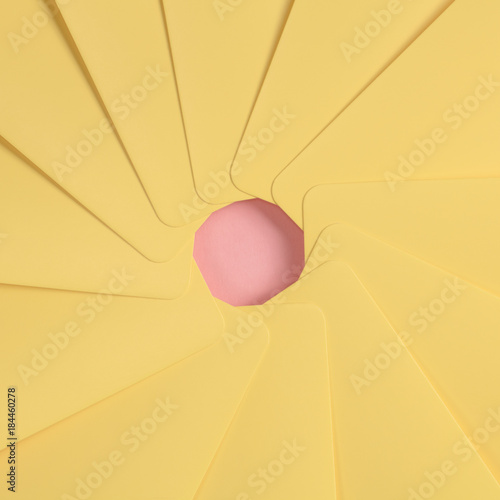 The simbol of an aperture of a camera is made from yellow paper on the pink background.