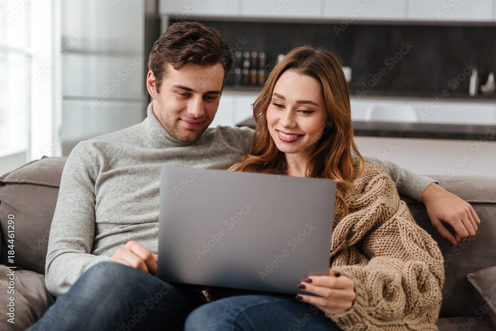 Happy loving coupe sitting on sofa at home using laptop. Happy loving coupe sitting on sofa at home using laptop.