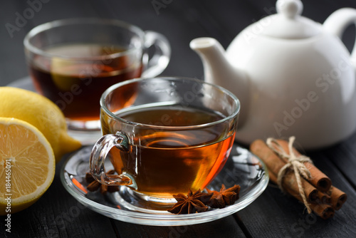 Spicy hot black tea in glass cup with lemon, cinnamon and star anise on black background