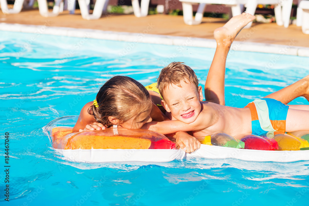 Little children playing and having fun in swimming pool with air mattress. Kids playing in water. Swimming concept. Boy and girl swim in resort pool during vacations