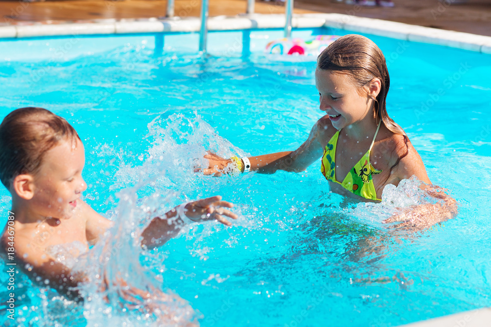 Little children playing and having fun in swimming pool with air mattress. Kids playing in water. Swimming concept. Boy and girl swim in resort pool during summer