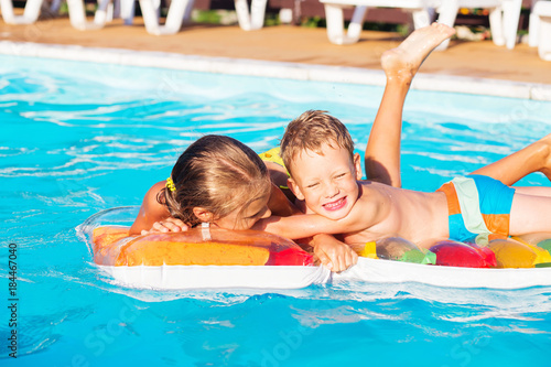 Little children playing and having fun in swimming pool with air mattress. Kids playing in water. Swimming concept. Boy and girl swim in resort pool during vacations © nata_zhekova