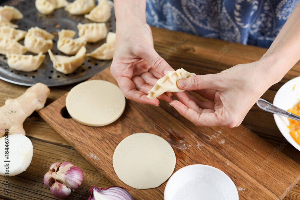 Closeup of woman hands making traditional Asian crescent shape steam dumplings on rustic wooden background