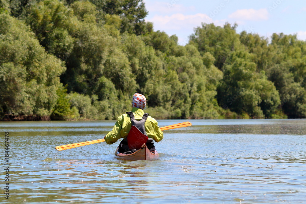 Man in brown wooden handmade kayak paddling at river on biosphere reserve in spring. Kayaking in Danube river