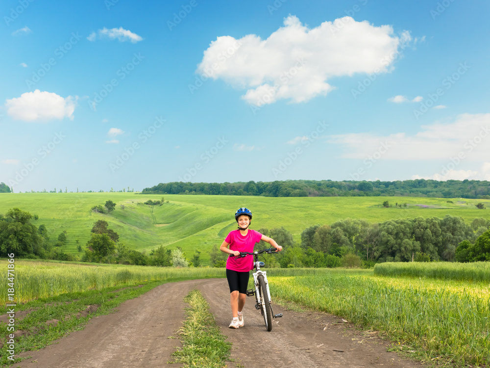 Fototapeta premium Sporty girl with bicycle in green field.