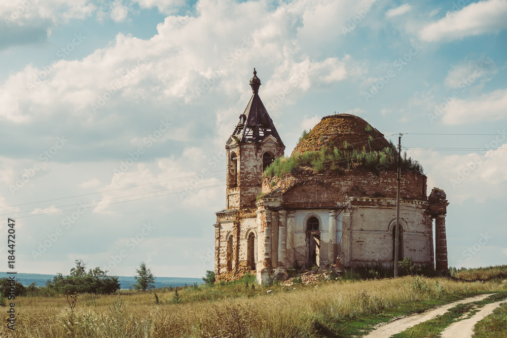 Ancient ruined Russian church or temple overgrown with grass among field