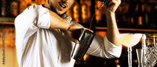 Obraz na plátně The incendiary bartender beautifully pours alcohol from the bottle into the shaker and arranges for his guests the present flaring of the show