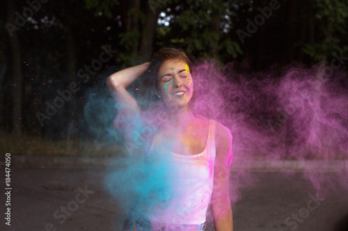 Joyful young woman with short hair posing with exploding Holi pink and blue dry powder