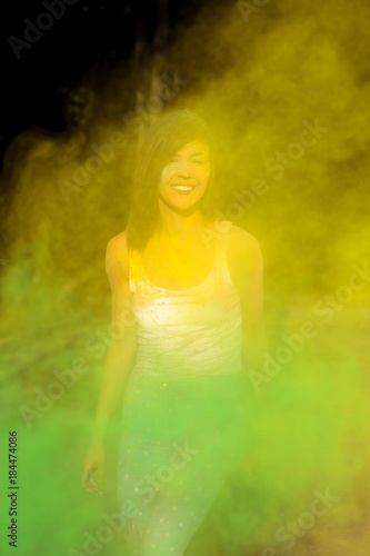Happy brunette woman with short hair playing with exploding green and yellow Holi paint