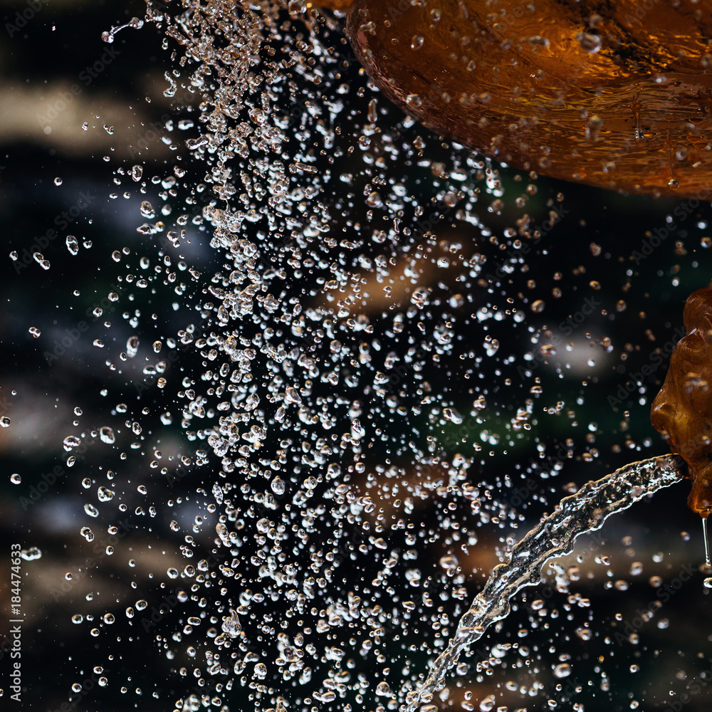 many water droplets fly from the fountain of golden color, the droplets have different shapes