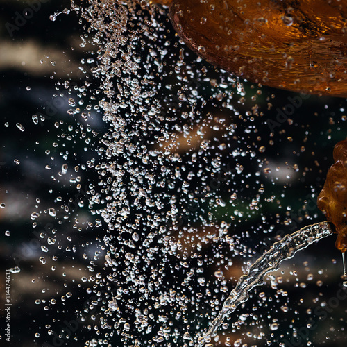 many water droplets fly from the fountain of golden color, the droplets have different shapes