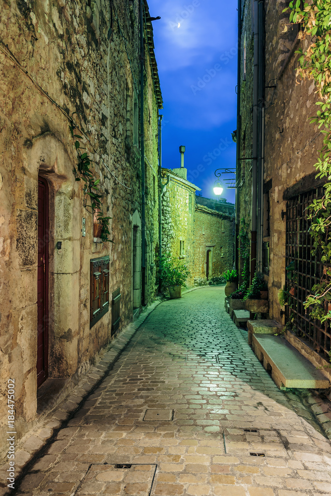 Narrow cobbled street with flowers in the old village at night, France.