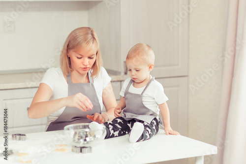 Young happy family in the domestic kitchen. Mother and child son preparing the dough, bake cookies, they smiling while spending time together