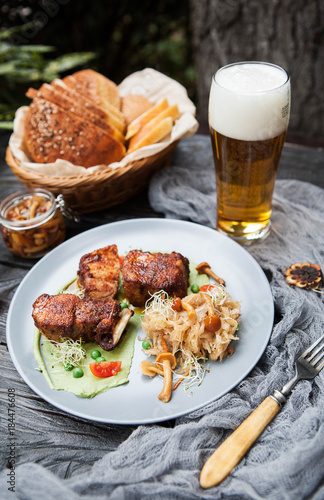 rustic composition: pork on grill on pea puree with stewed cabbage and mushrooms with a glass of beer on a wooden table