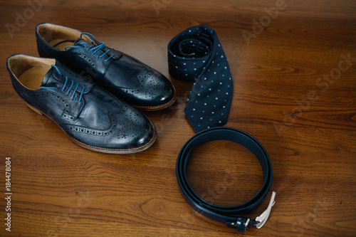 Black leather shoes, golden watch, wooden bow tie and belt stand on the wooden floor