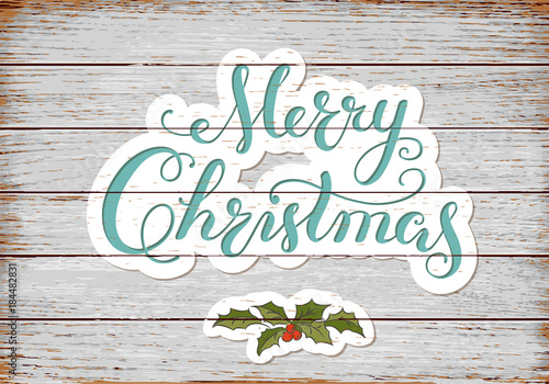 Calligraphy Lettering MERRY CHRISTMAS with hand drawn elements on old rustic planks. Holly branch.