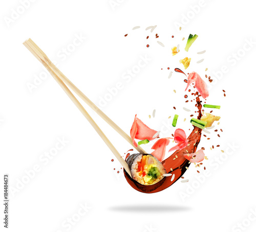 Piece of sushi sandwiched between chopsticks with splashes of soy sauce, isolated on white background