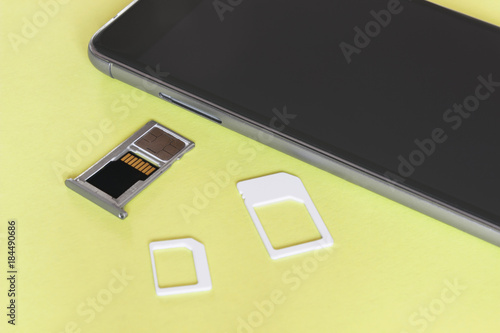Adapters on a SIM card from larger to nano-sim with a SIM card in the slot near and a memory card with a phone on a yellow background, close up	