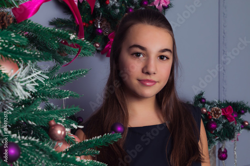 Pretty teenage girl decorates a Christmas tree. Merry Christmas and Happy New Year.