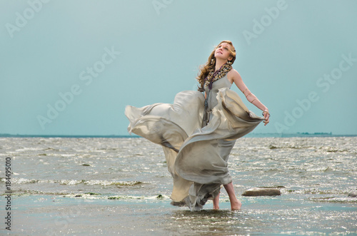 woman in a silk dress in the wind stands in the shallow water