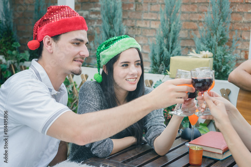 Group young people having drink and fun in santa hats throwing colorful on celebrating new year or christmas party, exchanging presents