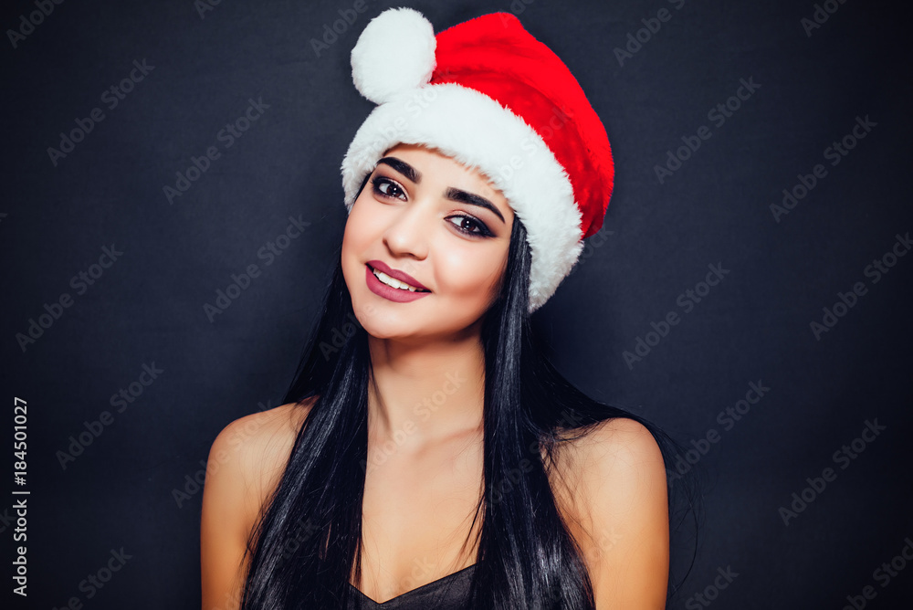 Beautiful woman with black straight hair and a Santa Claus hat on a dark background smiling. Close-up. Space for text
Beautiful woman with black straight hair and a Santa Claus hat on a dark background smiling. Close-up. Space for text