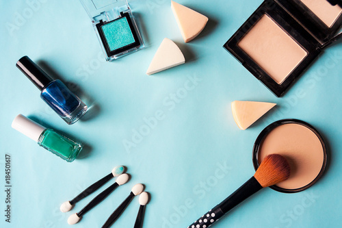 A set of cosmetics: blush, nail polish, shadows, brushes and powder on a blue background. Girls' Accessories. Flat lay with place for text