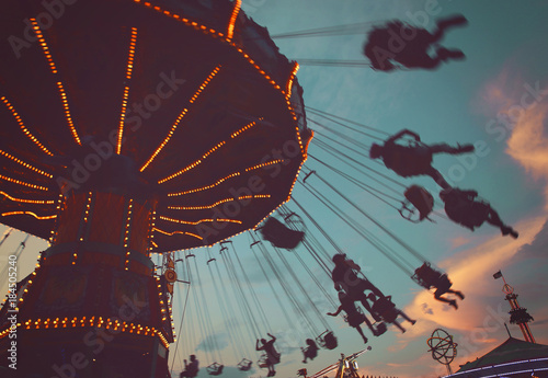  local fair at dusk with people riding swinging rides and enjoying the summer atmosphere toned with a retro vintage instagram filter app or action