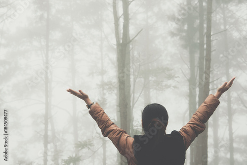 woman raise hand with fog and mist in pine tree forest. people, travel, nature concept