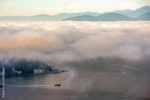 A Foggy morning in Seattle over Puget sound with a boat below and the Olympic Mountains above