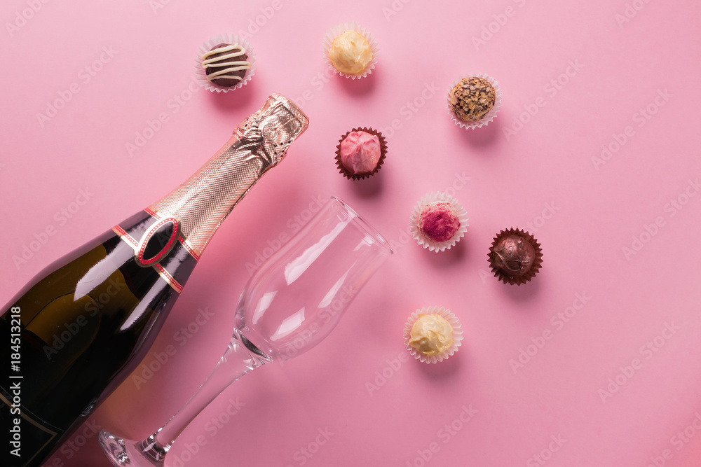 Sweets of dark and white chocolate, a bottle of champagne and a glass on a pink background. Celebratory concept. Sweets of dark and white chocolate, a bottle of champagne and a glass on a pink background. Celebratory concept.