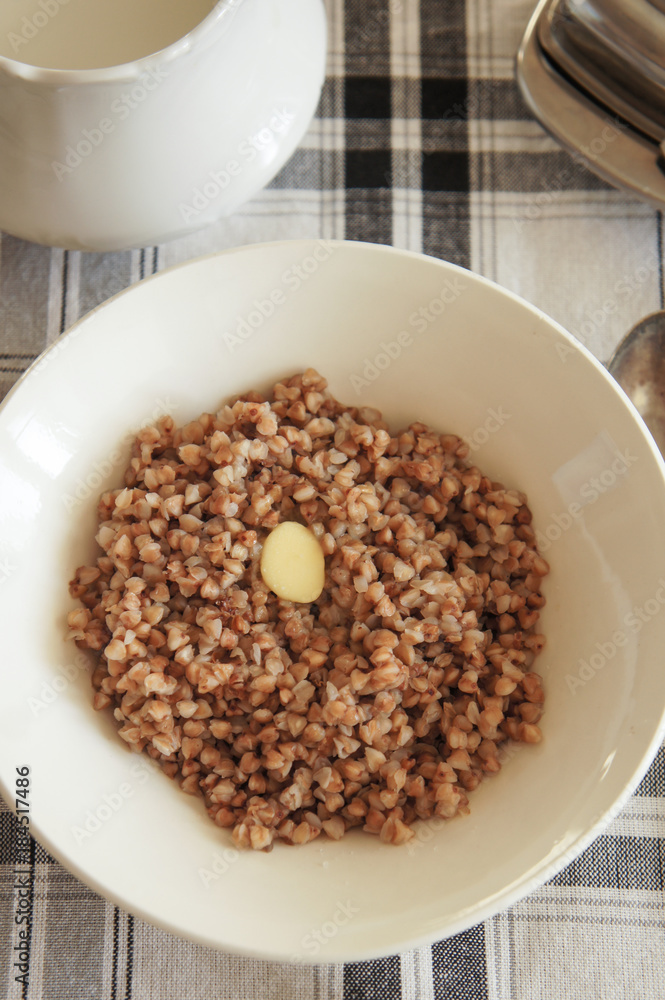 Boiled buckwheat with butter in white plate on checked table-cloth vertical Boiled buckwheat with butter in white plate on checked table-cloth vertical