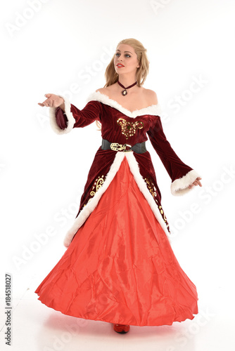 full length portrait of pretty blonde lady wearing red and white christmas inspired costume gown, standing pose on white background. © faestock