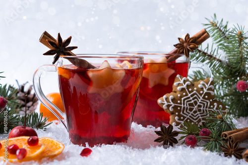 Hot mulled spiced red wine in glass mug with with festive decoration lights and gingerbread . On white snow background