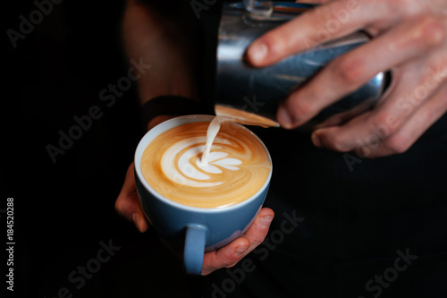 Barista making coffee with latte art, selective focus on dark background. Hand of barista making latte or cappuccino coffee pouring milk making latte art. Latte art coffee.