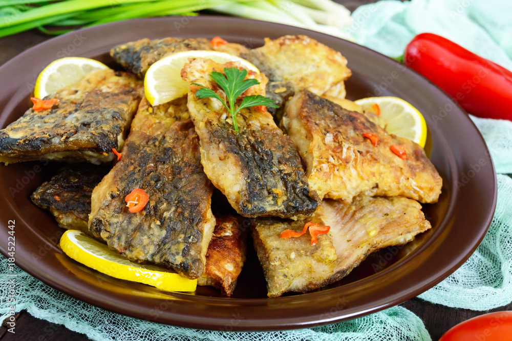 Pieces of fried fish (carp) on a ceramic plate on a dark wooden background. Pieces of fried fish (carp) on a ceramic plate on a dark wooden background.