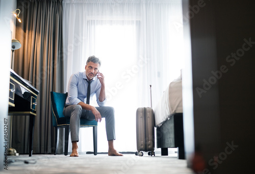 Mature businessman with smartphone in a hotel room.