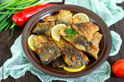 Pieces of fried fish (carp) on a ceramic plate on a dark wooden background.