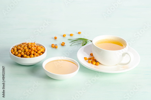 Sea buckthorn in porcelain bowl  honey and cup of  tea with Sea buckthorn on blue table. top view
